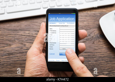 Nahaufnahme der Person Hände füllen Online Bewerbung auf Handy am Schreibtisch Stockfoto