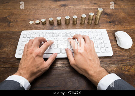 Nahaufnahme der Geschäftsmann Hand mit Tastatur Vor gestapelte Münzen Stockfoto