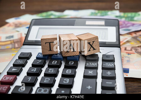 Nahaufnahme einer steuerlichen Wort auf Holzblöcken über Rechner auf Banknoten Stockfoto