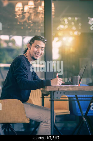 Asiatische jüngeren freier Mann zu Hause arbeiten im Büro mit Computer Laptop toothy Lächeln Stockfoto