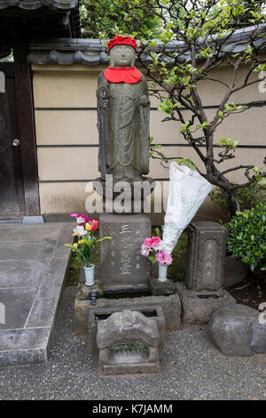 Tokyo, Japan - 15. Mai 2017: Friedliche Stein religiösen Jizo Statue mit Red Hat und mit frischen Blumen geehrt Stockfoto