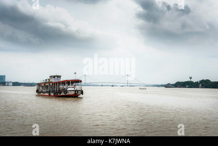 Öffentliche Fähre überquert den Hooghly River an einem bewölkten Monsunmorgen mit Blick auf die neue Howrah Brücke im Hintergrund in Kalkutta, Indien. Stockfoto