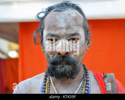 Indischer Hindu-Anhänger mit blutverschossen Augen und heiligem weißen Eschen (Vibhuti) im ganzen Gesicht posiert für die Kamera während Shivratri Mela. Stockfoto