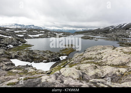 Typisch norwegische Landschaft mit schneebedeckten Bergen und Clear Lake in der Nähe der berühmten Aurlandsvegen (Bjorgavegen), Mountain Road, Aurland, Norwegen. Stockfoto