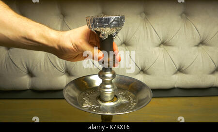 Rauch Shisha auf einem schwarzen Hintergrund mit einem schönen Rauch. Braun shisha Schüssel für Tabak mit langem Bein. Vorbereiten der Shisha, nargile Shisha aka oder in einem Restaurant, indem Sie den Holzkohlen auf der Oberseite. Stockfoto
