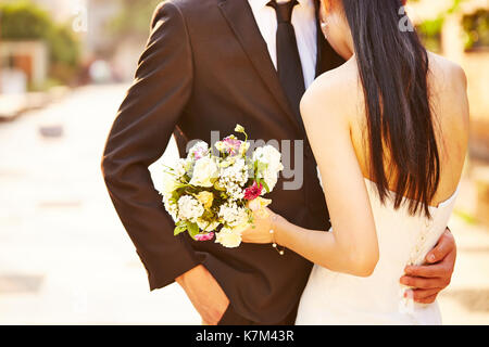 Liebende Braut und Bräutigam mit Blumenstrauß am Tag der Hochzeit umarmte. Stockfoto