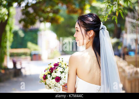 Schöne und glückliche junge asiatische Braut tragen Bridal Veil Holding ein Bündel von Blume, Ansicht von hinten. Stockfoto