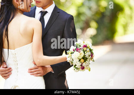 Asiatische Hochzeit paar Umarmen, konzentrieren sich auf die Bouquet. Stockfoto