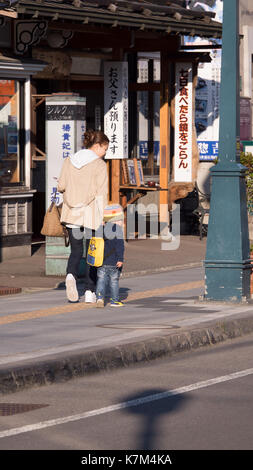 Käufer vorbei gehen traditionelle Storefront in Otaru Japan. Historische Gebäude aus Stein mit touristischen Informationen Zeichen vor. Orange Holz- Kanji Stockfoto