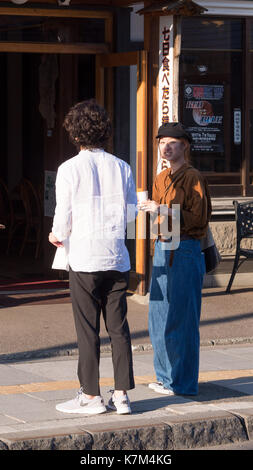 Jungen japanischen Paar gekleidet in modischen Jeans, Schwarzes und weißes Hemd in der späten Nachmittagssonne auf dem Bürgersteig stehen weg von suchen und an der Kamera. Stockfoto