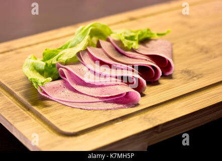 Dünn geschnittene Wurst mit grünem Salat auf Holzbrett Stockfoto