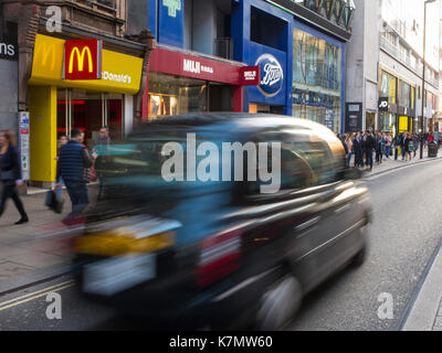 Ein unscharfer Taxi passiert einen Zweig einer Chain Store in London Stockfoto