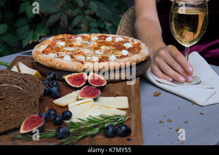 Pizza an Bord, Käse, Brot. Frau hält ein Glas Wein. Stockfoto