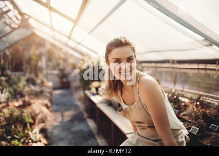 Porträt der jungen Frau im Gewächshaus. Schöne Gärtner an Gärtnerei sitzen. Stockfoto