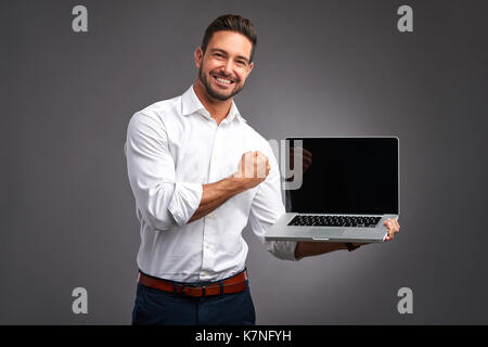 Ein hübscher junger Mann hält und zeigt den Bildschirm eines Laptops und feiern Stockfoto