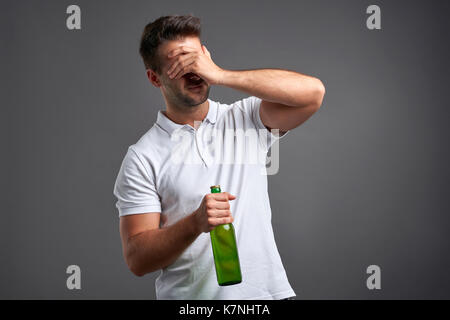 Ein hübscher junger Mann Gefühl verzweifelt und packte seinen Kopf halten Sie ein Bier Stockfoto
