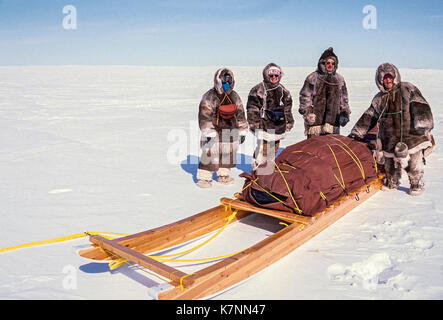 Besucher gekleidet in traditionelle Caribou haut Kleidung stand neben einem traditionellen Inuit cargo Schlitten, genannt eine komatik. Stockfoto