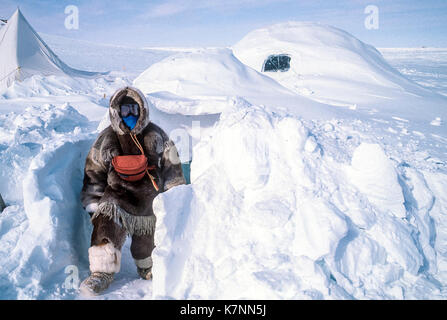 Besucher in traditionellen Caribou haut Kleidung kommt aus Iglu, wo Sie Camping für mehrere Tage wurde. Hinweis Fenster in Zurück aus einem Block von Clear Ice gemacht. Stockfoto