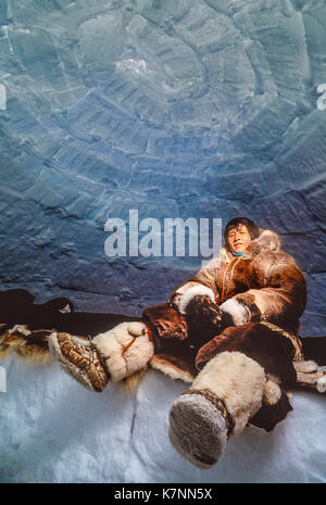 Besucher in traditionellen Caribou haut Kleidung sitzt auf Caribou Skins auf eine schlafende Sims im Iglu, wo sie Campingplatz für eine Woche. Außerhalb Baker Lake, Nunavut, Kanada. Stockfoto