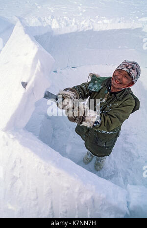 Inuit ältester Mann, Mitte der 60er Jahre, in der modernen Winter Kleidung, Schnitte Eisblöcke mit Messer und schneidet sie während Gebäude im traditionellen Iglu. Stockfoto