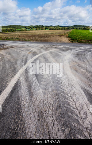 Muddy Reifenspuren auf Risse Fahrbahn vom Bauernhof Fahrzeuge - Frankreich. Stockfoto