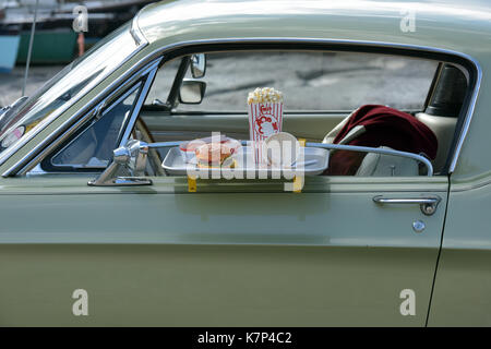 Ein Beef Burger und Pommes an die Tür eines klassischen Amerikanischen Auto auf eine Fahrt durch Gerichte zum Mitnehmen oder im Kino mit Popcorn. Fast Food Restaurants Stockfoto