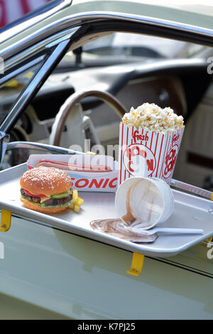 Ein Beef Burger und Pommes an die Tür eines klassischen Amerikanischen Auto auf eine Fahrt durch Gerichte zum Mitnehmen oder im Kino mit Popcorn. Fast Food Restaurants Stockfoto