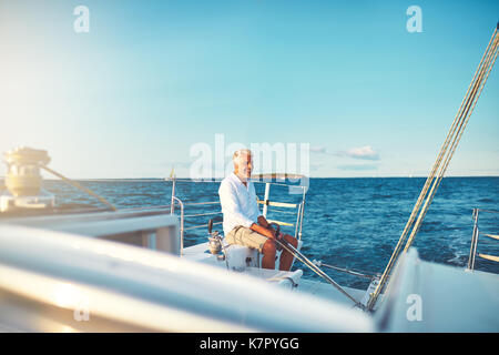 Lächelnd reifer Mann sitzen auf dem Deck des Schiffes beim Segeln entlang der Küste an einem sonnigen Tag Stockfoto