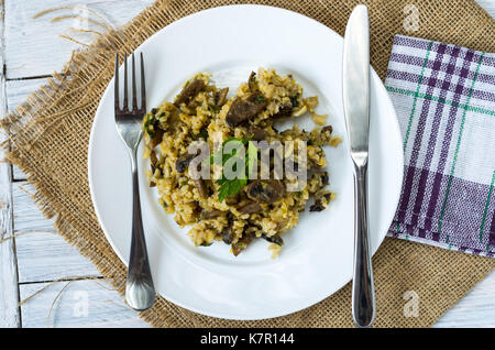 Risotto in eine weiße Platte und mit Küchengeräten auf Entlassung. Im rustikalen Stil. Stockfoto