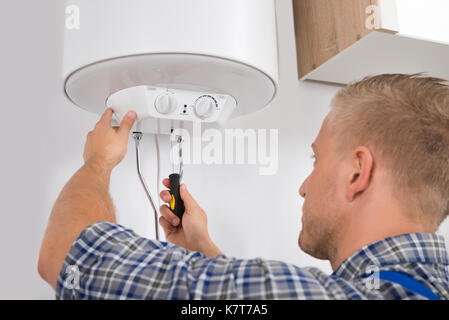 Junge männliche Arbeiter zur Festsetzung elektrischer Boiler mit Schraubendreher Stockfoto