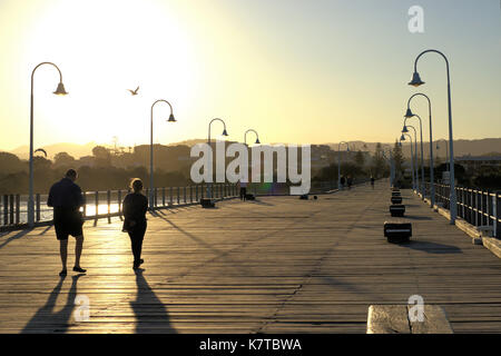 Goldene stunde Australien. Sonnenuntergang gesehen von Jetty in Coffs Harbour, Urlaub, Australien. Menschen zu Fuß Straße Lampen, Holzbank, etc. Stockfoto