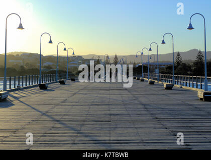 Goldene stunde Australien. Sonnenuntergang gesehen von Jetty in Coffs Harbour, Urlaub, Australien. Menschen zu Fuß Straße Lampen, Holzbank, etc. Stockfoto