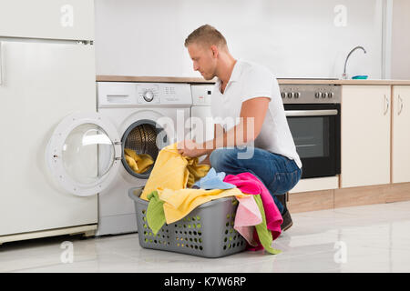 Jungen gutaussehenden Mann, schmutzige Wäsche in die Waschmaschine zu Hause Stockfoto