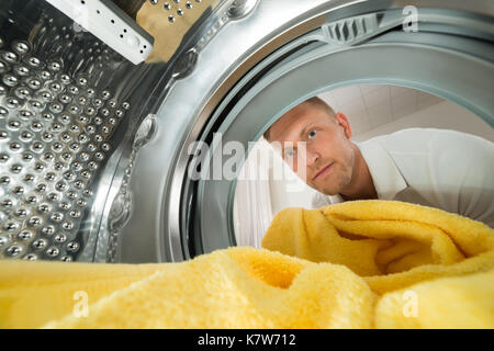 Junger Mann, Gelb Handtuch Blick aus der Waschmaschine Gerät Stockfoto