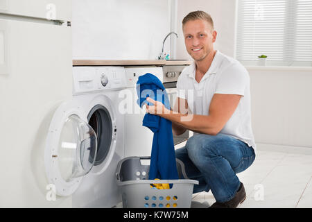 Mann mit Wäschekorb Laden Waschmaschine mit Kleidung in der Küche Zimmer Stockfoto