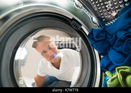 Portrait des jungen Mannes, Ansicht von Innen die Waschmaschine mit Kleidung Stockfoto