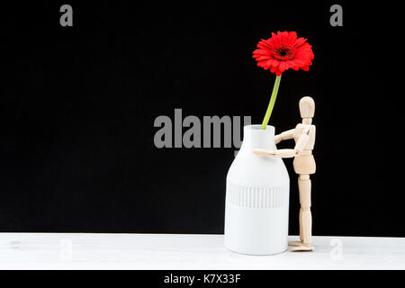 Holz Schaufensterpuppe mit einer Vase und rote Blume. Es ist Platz auf der linken Seite. Stockfoto