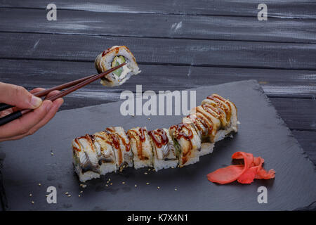 Sushi-roll auf eine schwarze Platte mit Mann Hand in Stäbchen eine Rolle auf schwarzem Hintergrund Stockfoto