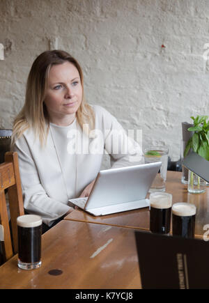 Junge geschäftsfrau an den hölzernen Tisch in der Bar in einen Tablet-PC auf dem Schreibtisch hören Freunde Stockfoto