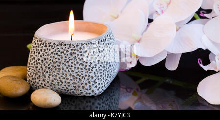 Spa Kerze mit Orchideen und Massage Steine Stockfoto