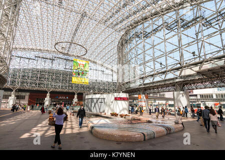 Kanazawa Station, Japan. Innenraum der berühmten Wahrzeichen Motenashi Kuppel mit großen Poster hängen, Leute, Sitzecke, tagsüber, blauer Himmel. Stockfoto