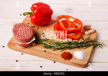 Rohes Hackfleisch burger Schnitzel mit roten Zwiebeln, Knoblauch, Oliven und Paprika Öl auf einem weißen Holz- Hintergrund Stockfoto