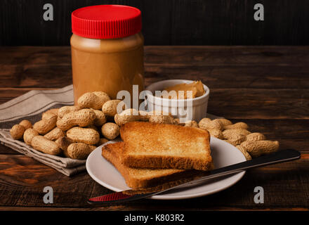 Peanut butter Sandwiches oder Toasts mit Jar und Erdnüsse in der Schale auf einem schwarzen Holz- Hintergrund Stockfoto