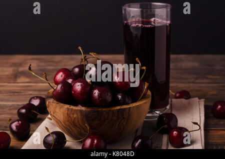 Frische Kirschen auf Holztisch mit Wassertropfen und Kirschsaft, rustikal, dunkel Stockfoto