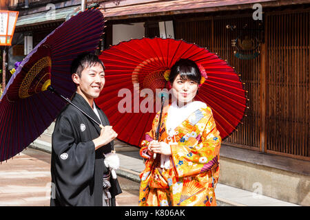 Lächelndes Paar, in 20s, das Tragen von Kimonos und Holding Sonnenschirme, stehend in der berühmten Straße in Higashi Chaya Bezirk von Kanazawa, Japan. Stockfoto