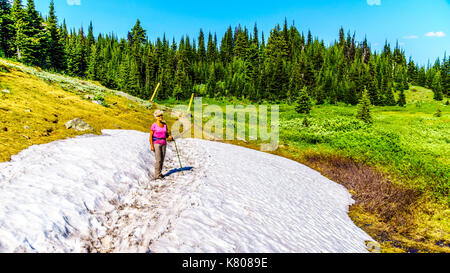 Ältere Frau wandern durch einen Patch von Schnee von Almen in den Alpen in der Nähe des Dorfes Sun Peaks in der Shuswap Highlands Stockfoto