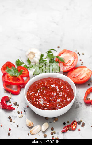 Tomatensauce in einer weißen Schüssel, frischen Tomaten und Petersilie auf grauem Beton Hintergrund. Ansicht von oben Stockfoto