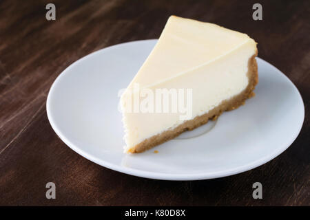 Plain Käsekuchen Slice auf weiße Platte auf Holztisch. Detailansicht, selektiver Fokus, horizontal Stockfoto