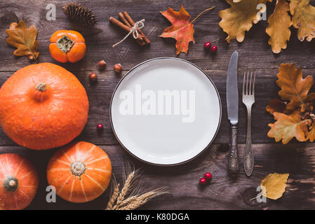 Herbst oder Thanksgiving Day Tabelle einstellen. Laub, Kürbisse, Gewürze, leeren Teller und Besteck auf Holztisch. Ansicht von oben, getönten Bild Stockfoto