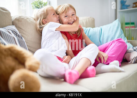 Süße blonde Mädchen im Geheimen mit ihrem Lächeln ältere Schwester beim verbringen Wochenende zusammen im gemütlichen Wohnzimmer Stockfoto